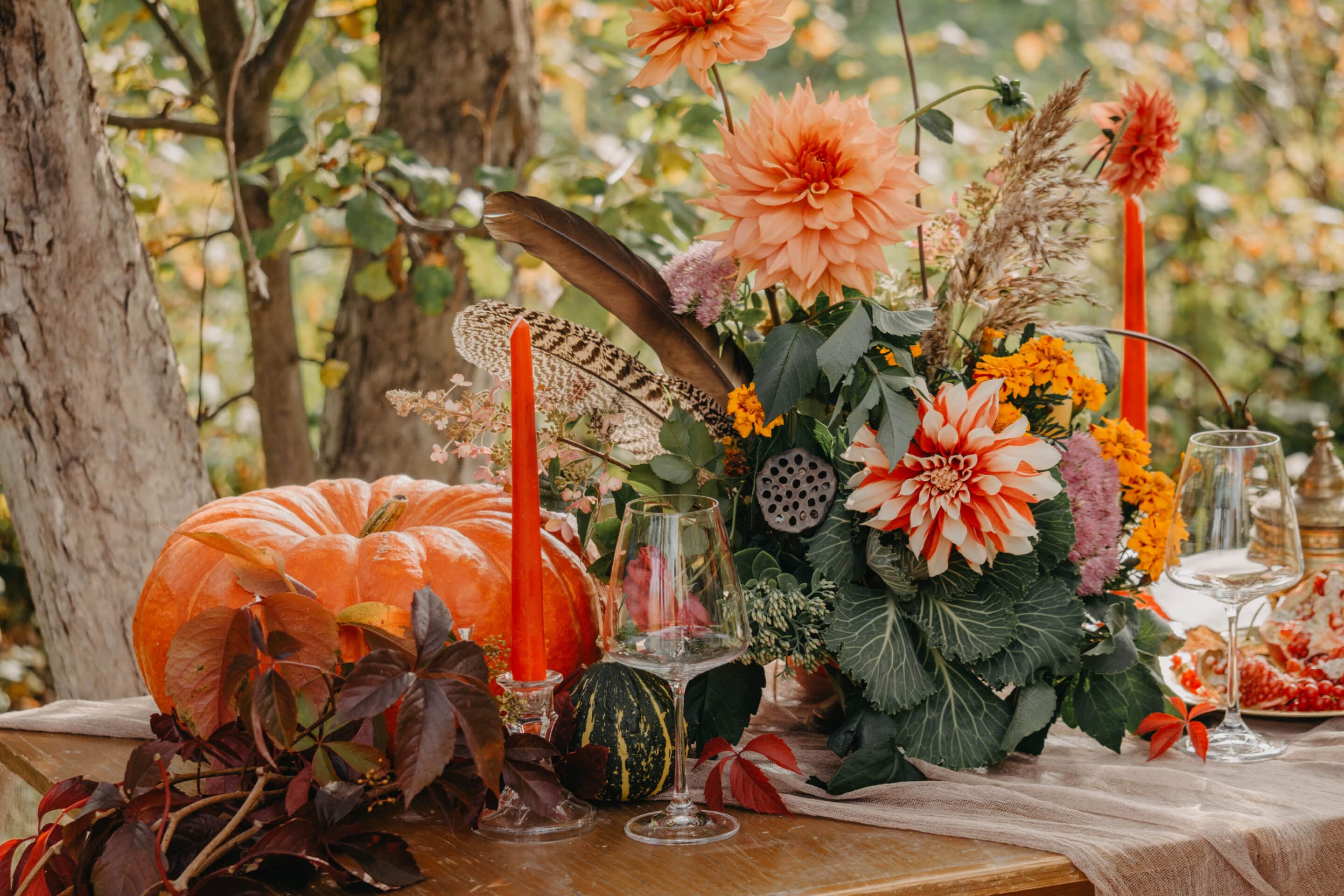 Autumn romantic setting: Bouquet of dahlias, pomegranates, candles, pumpkins and glasses